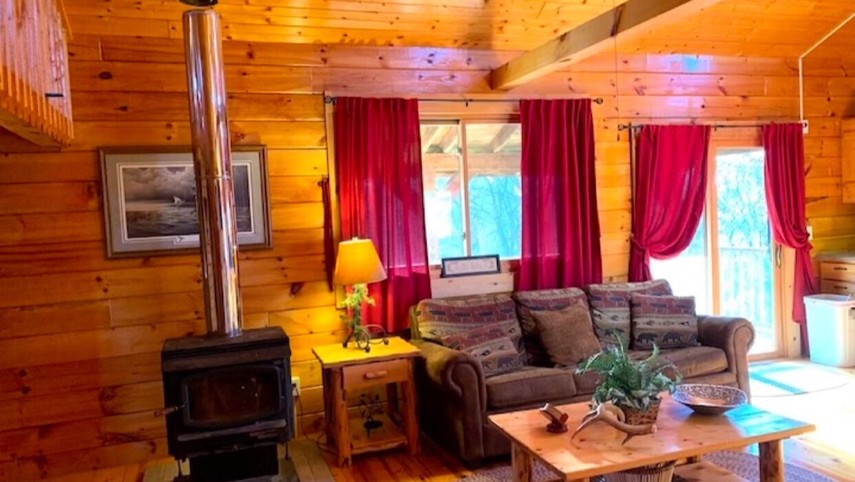 L’intérieur d’un chalet en bois, avec une cheminée, un canapé, une table et des rideaux rouges.
