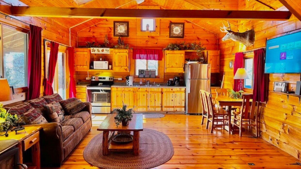 Ein gemütliches Blockhaus-Interieur mit Holzvertäfelung, einem Essbereich, einer Küche und einem Wohnzimmer mit Sofa und Couchtisch.