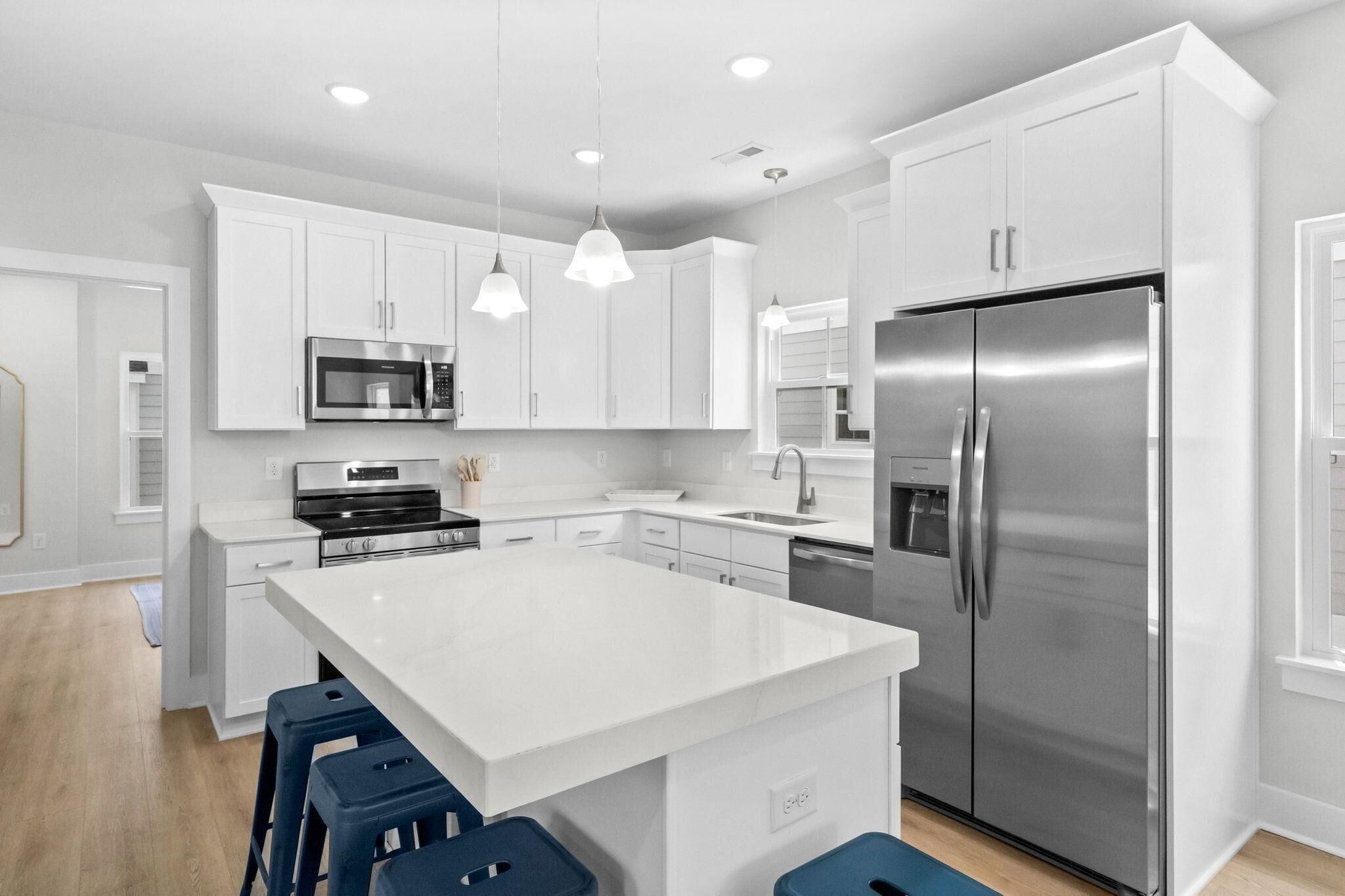 A modern kitchen with white cabinetry, stainless steel appliances, and blue bar stools.