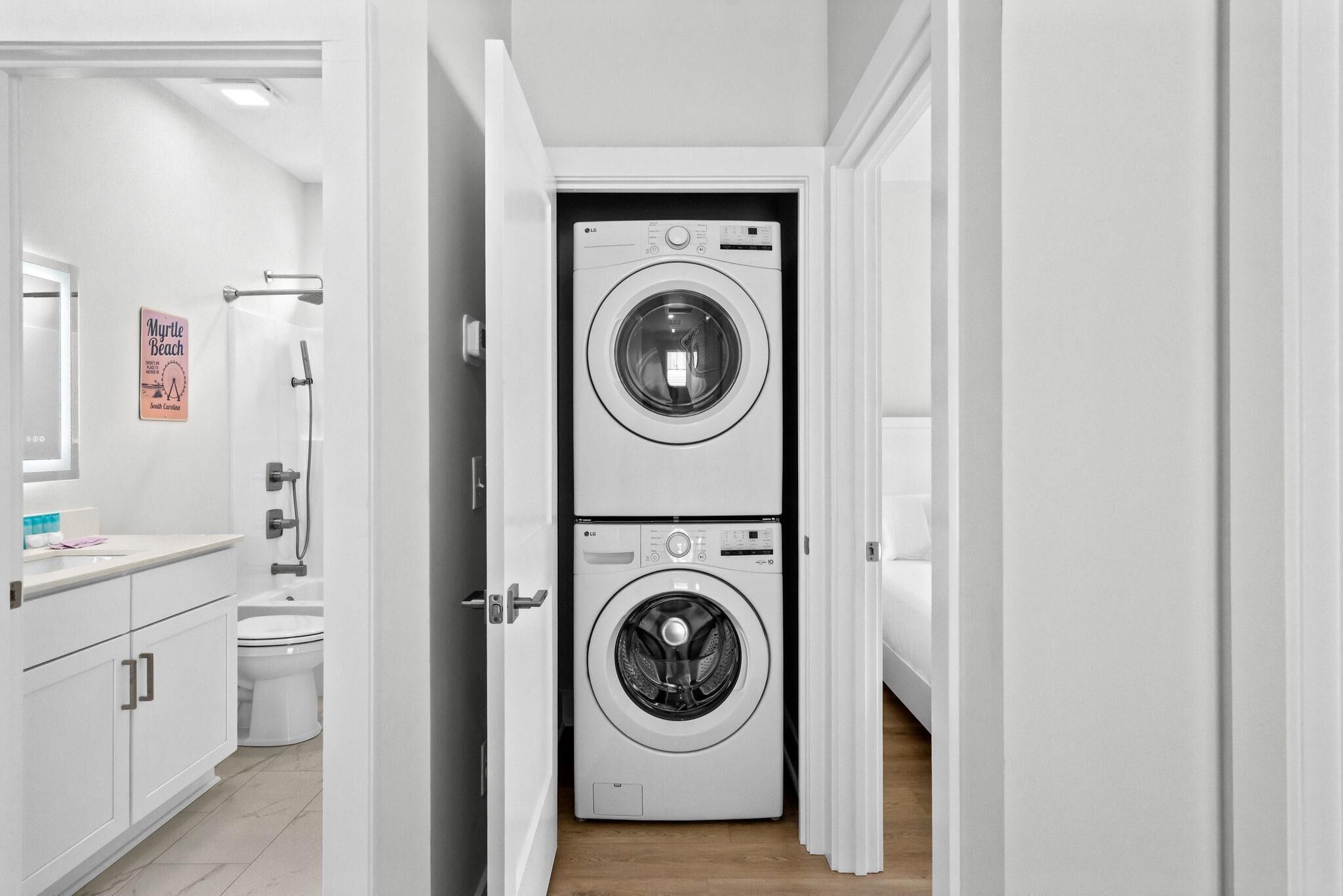 A laundry room with two stacked front-loading washing machines, a shower area, and a toilet.