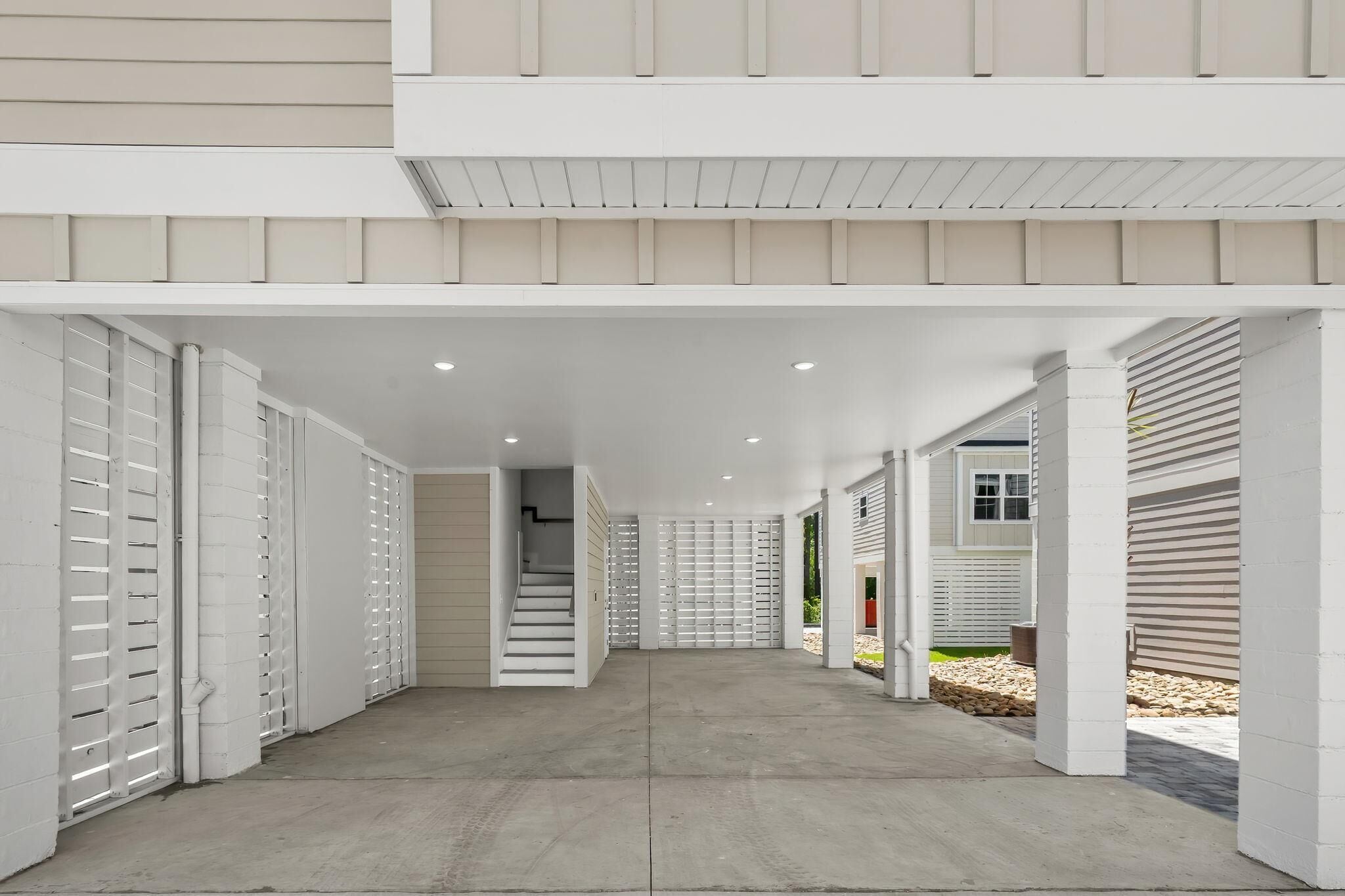 A covered outdoor corridor with white walls and a concrete floor, leading to a staircase.