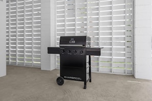 A black Charbroil grill with four burners and a side shelf, positioned in a room with white walls and a concrete floor. - Boardwalk Bliss 2.5 Blocks to Ocean Pet Friendly (Myrtle Beach)