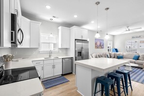A modern kitchen with white cabinetry, a stainless steel refrigerator, and a central island with bar stools. - Boardwalk Bliss 2.5 Blocks to Ocean Pet Friendly (Myrtle Beach)