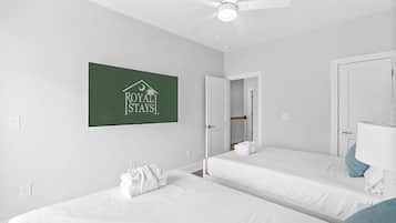 A hotel room with two beds, a ceiling fan, a sign reading 'ROYAL STAYS,' and a bathroom with a mirror and towel.