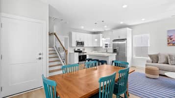 A modern kitchen with white cabinets, stainless steel appliances, and a wooden dining table with teal chairs.