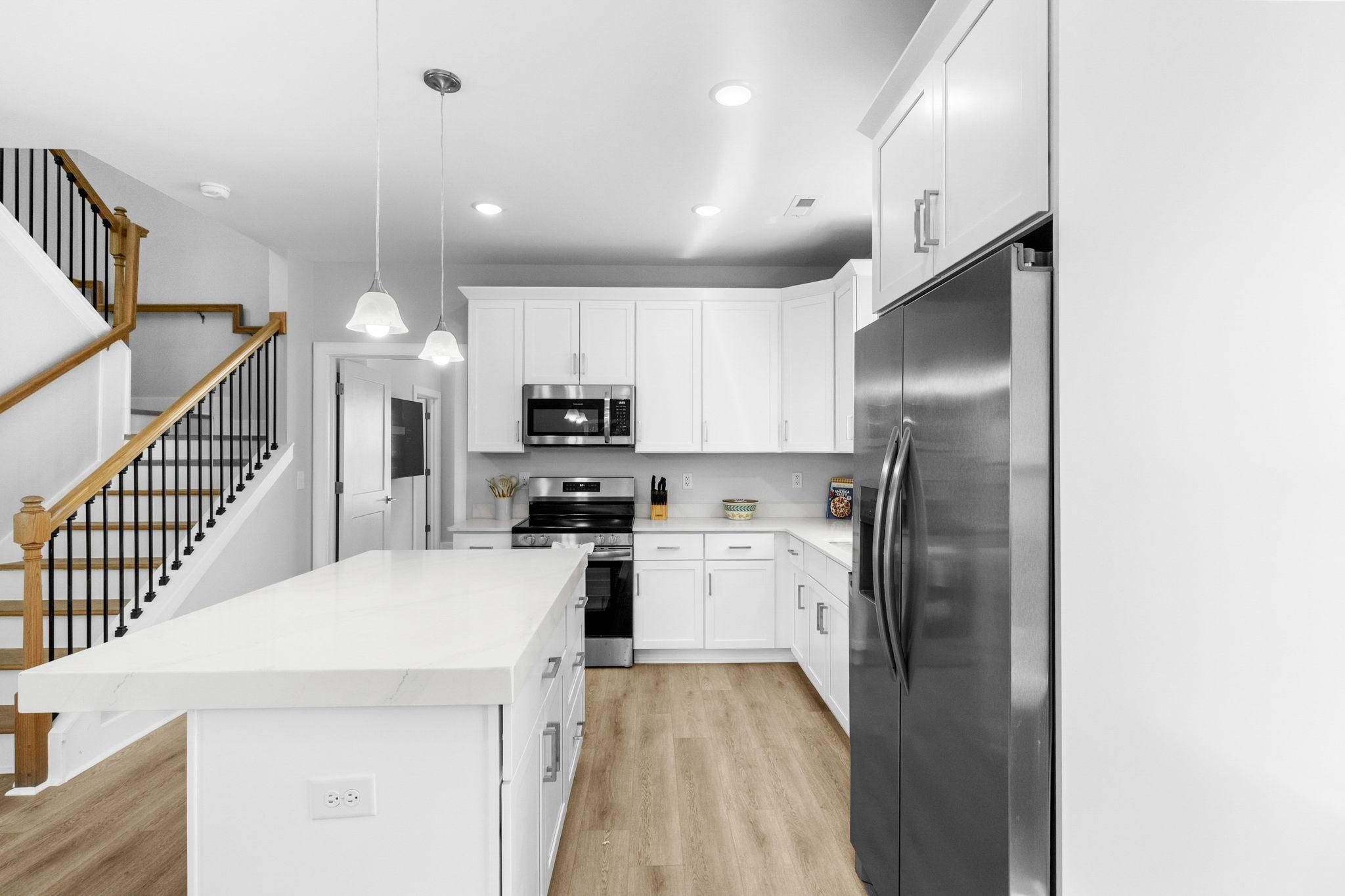 Una cocina moderna con armarios blancos, electrodomésticos de acero inoxidable y una escalera de madera.