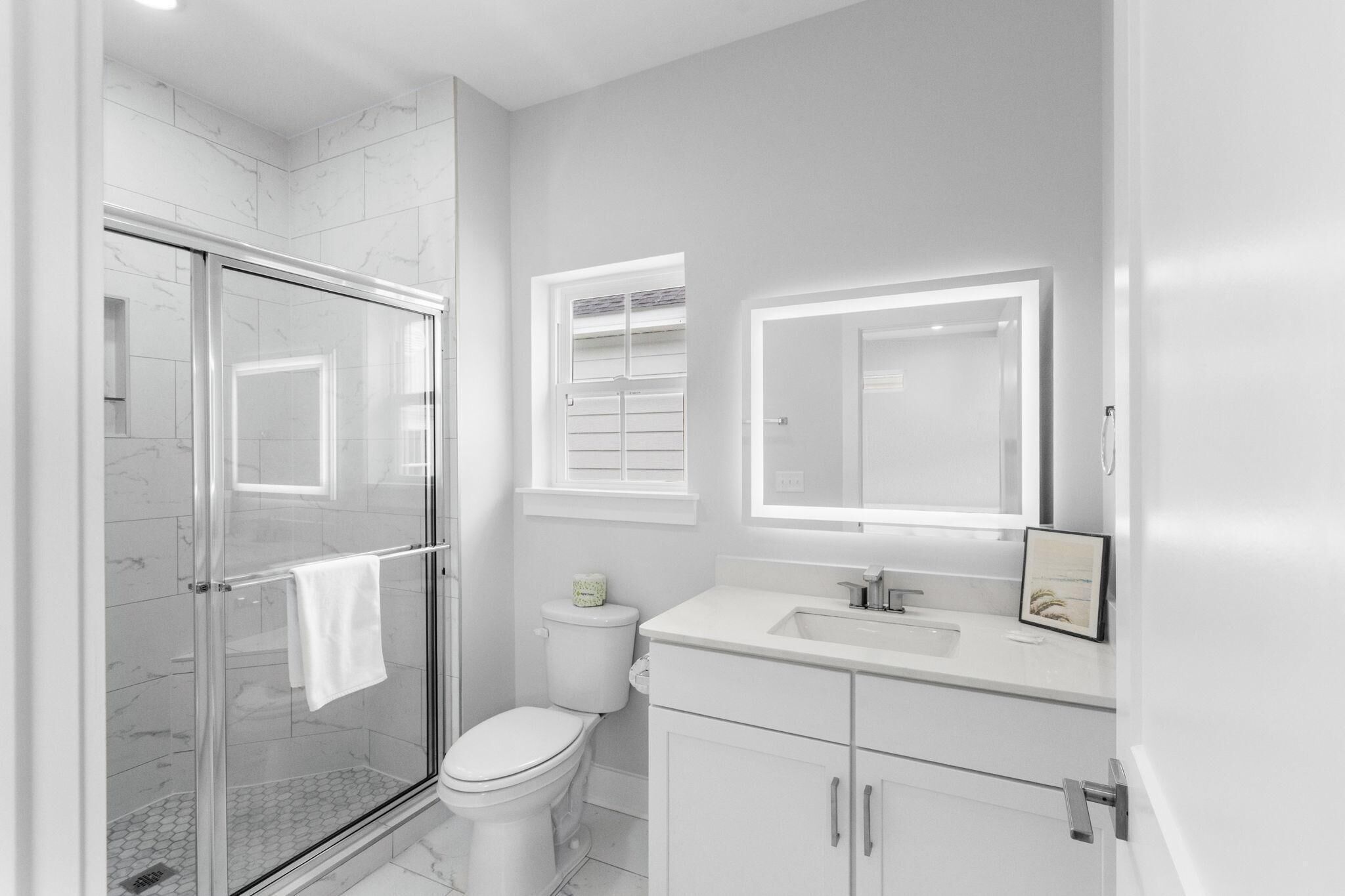 Une salle de bain moderne avec une douche à parois de verre, des toilettes, un lavabo et un miroir au-dessus du meuble-lavabo.