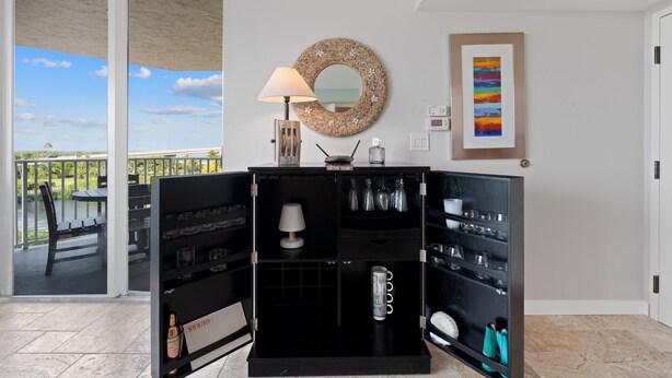 A room with a sliding glass door leading to a balcony, a black cabinet with shelves, a wall-mounted mirror, and a framed picture. - Lovers Key #508 (Fort Myers Beach)