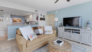 A living room with a beige sofa, a glass coffee table, a flat-screen TV, and a ceiling fan. - Lovers Key #508 (Fort Myers Beach)