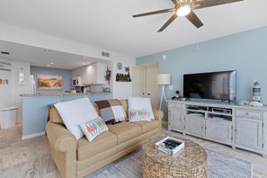 A living room with a beige sofa, a glass coffee table, a flat-screen TV, and a ceiling fan. - Lovers Key #508 (Fort Myers Beach)