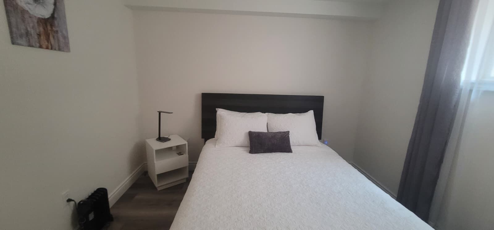 Una cama individual con cabecera oscura, una mesita de noche con lámpara y un estante pequeño.