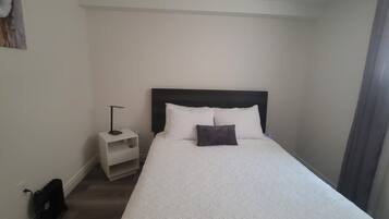 Una cama individual con cabecera oscura, una mesita de noche con lámpara y un estante pequeño.