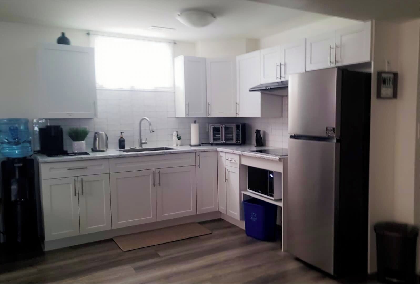 A modern kitchen with white cabinets, a stainless steel refrigerator, a microwave, and a water dispenser.