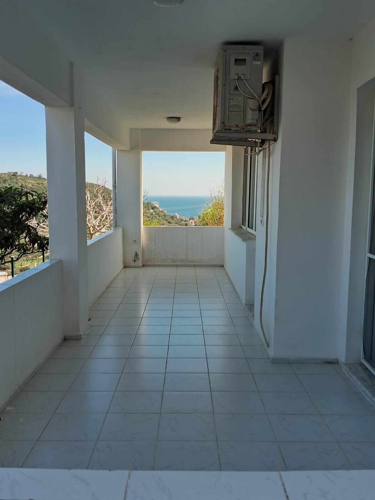 Un balcón con vista al mar, suelo de baldosas y un aire acondicionado de pared.