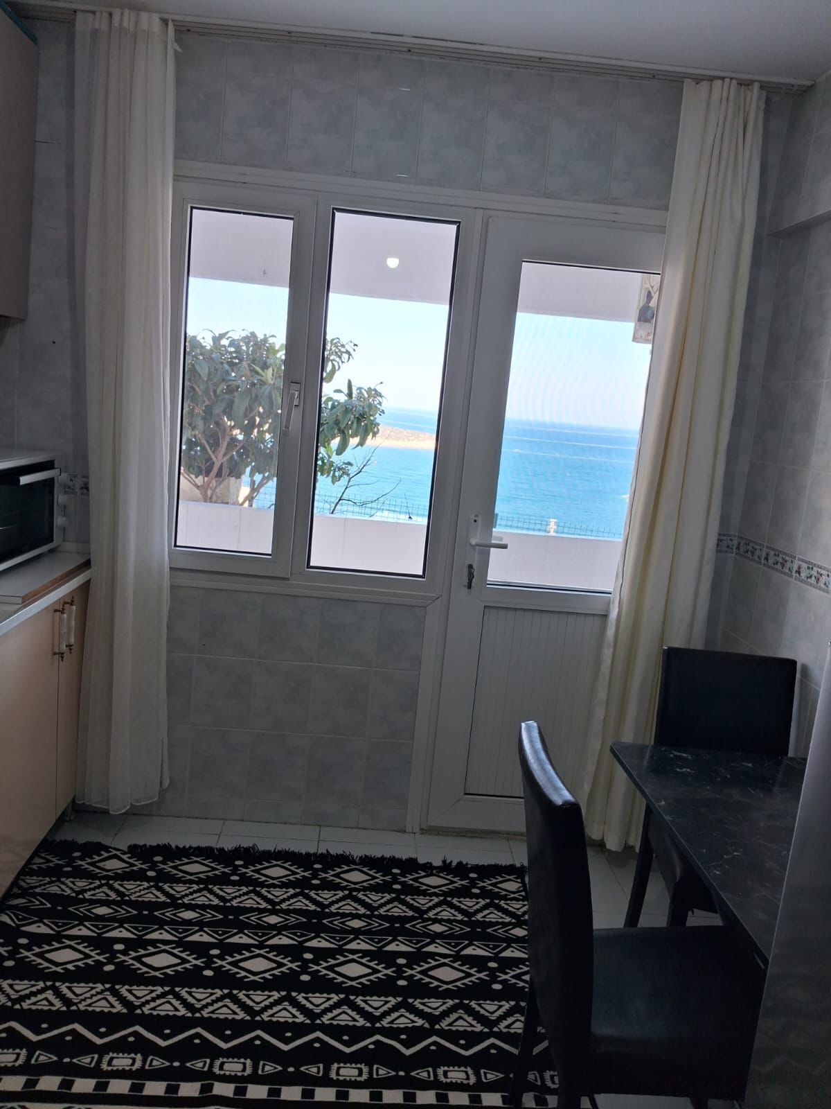 Une petite pièce avec vue sur la mer, un four à micro-ondes, une table à manger et un tapis à motifs.
