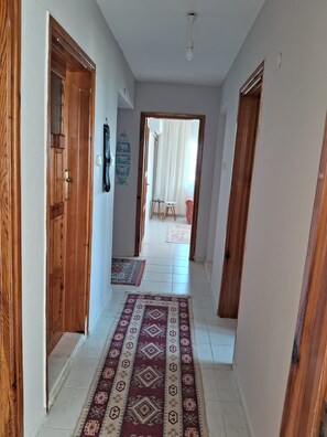 Un pasillo con puertas de madera, un tapete estampado y vista a una habitación con cama y cortinas.