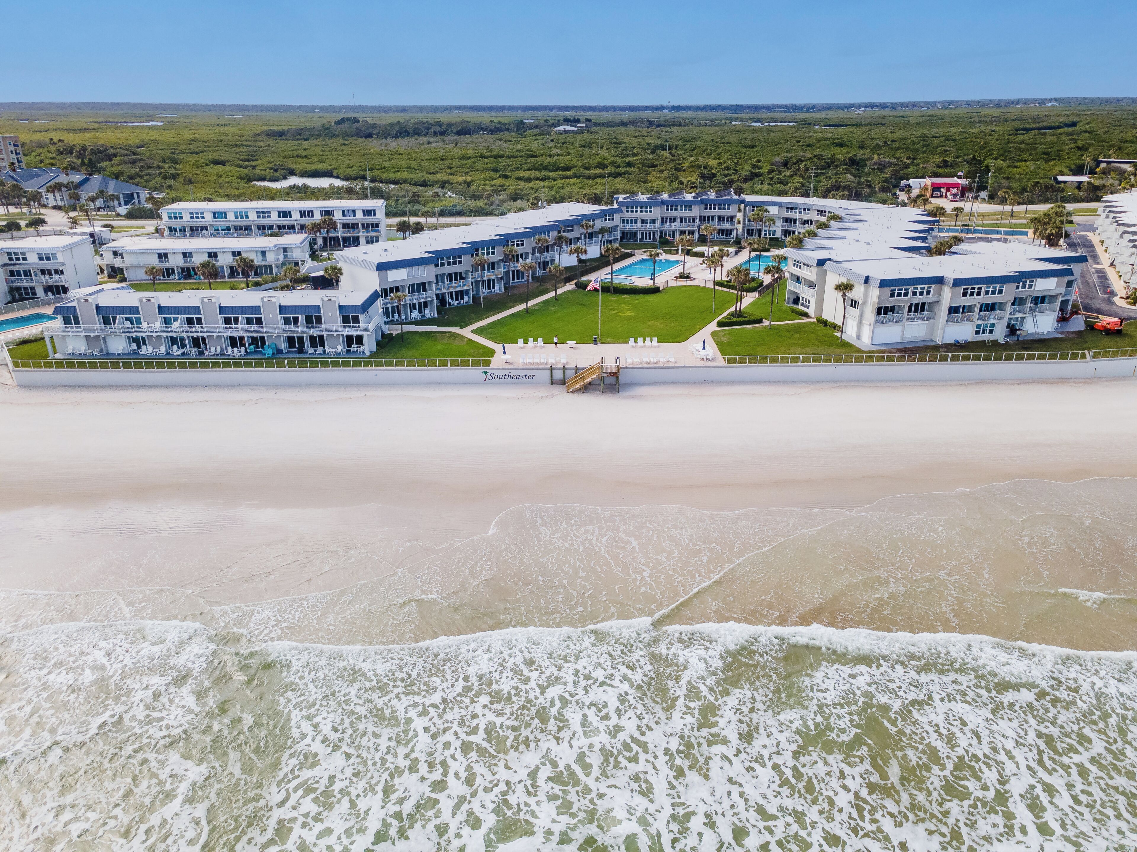 A beachfront hotel with multiple buildings, a swimming pool, and a beach in the foreground.