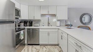 A modern kitchen with white cabinets, stainless steel appliances, and a marble floor. - 🦈Great Poolside View | Shuffleboard + Kiddie Pools | Southeaster E203 🌅 (New Smyrna  Beach)