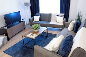 A modern living room with a flat-screen TV, two sofas, a coffee table, and a floor lamp. - Stylish City-Centre Apartment with Private Balcony (Wolverhampton)