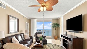 A living room with a ceiling fan, a large flat-screen TV, leather sofas, a coffee table, and a view of the ocean through a sliding glass door. - Palacio 1406 (Pensacola)