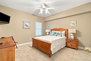 A bedroom with a wooden bed, a desk, a ceiling fan, and artwork on the walls. - Palacio 1406 (Pensacola)