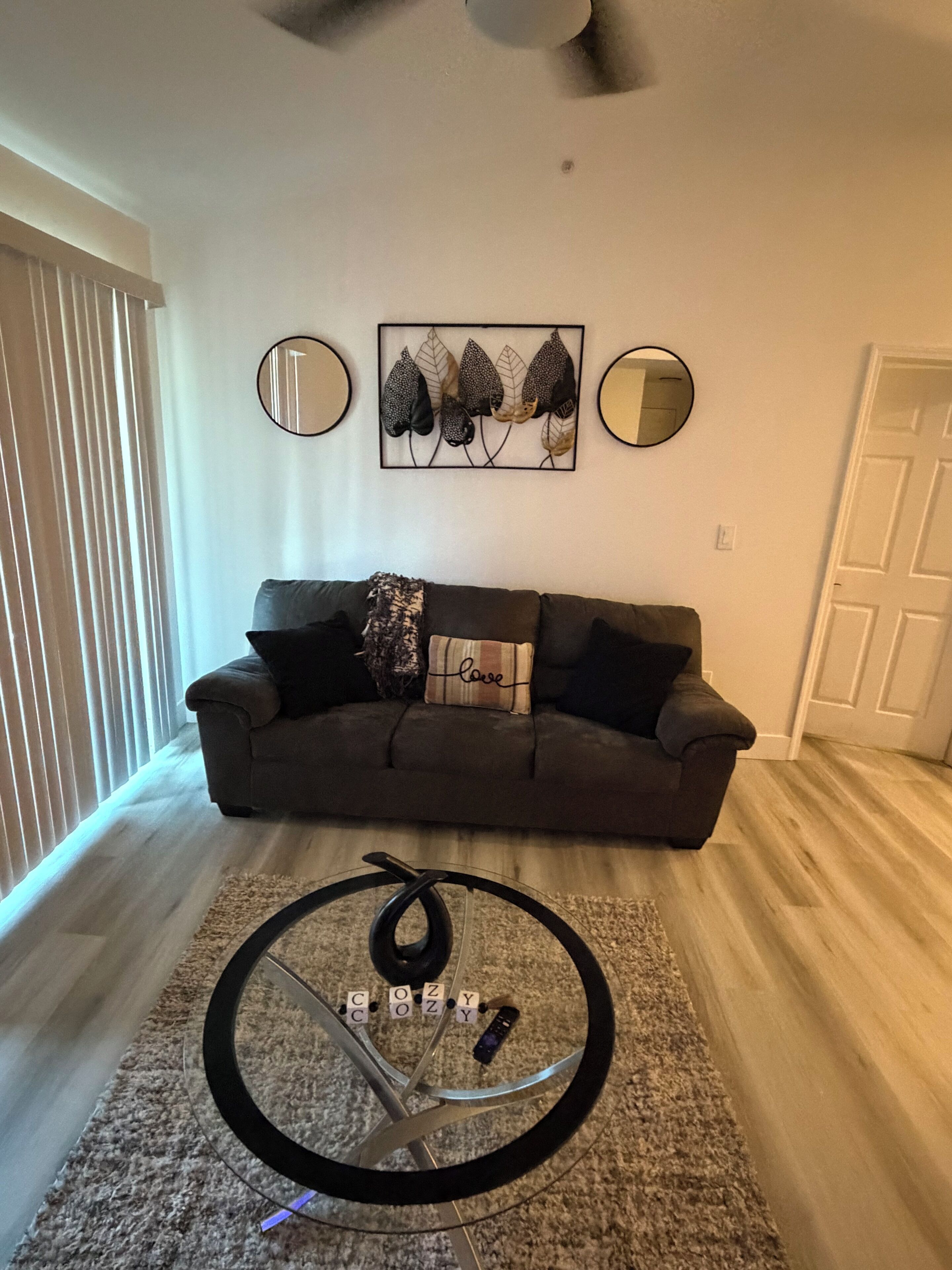 Un salon avec un canapé foncé, une table basse ronde et un miroir fixé au mur.