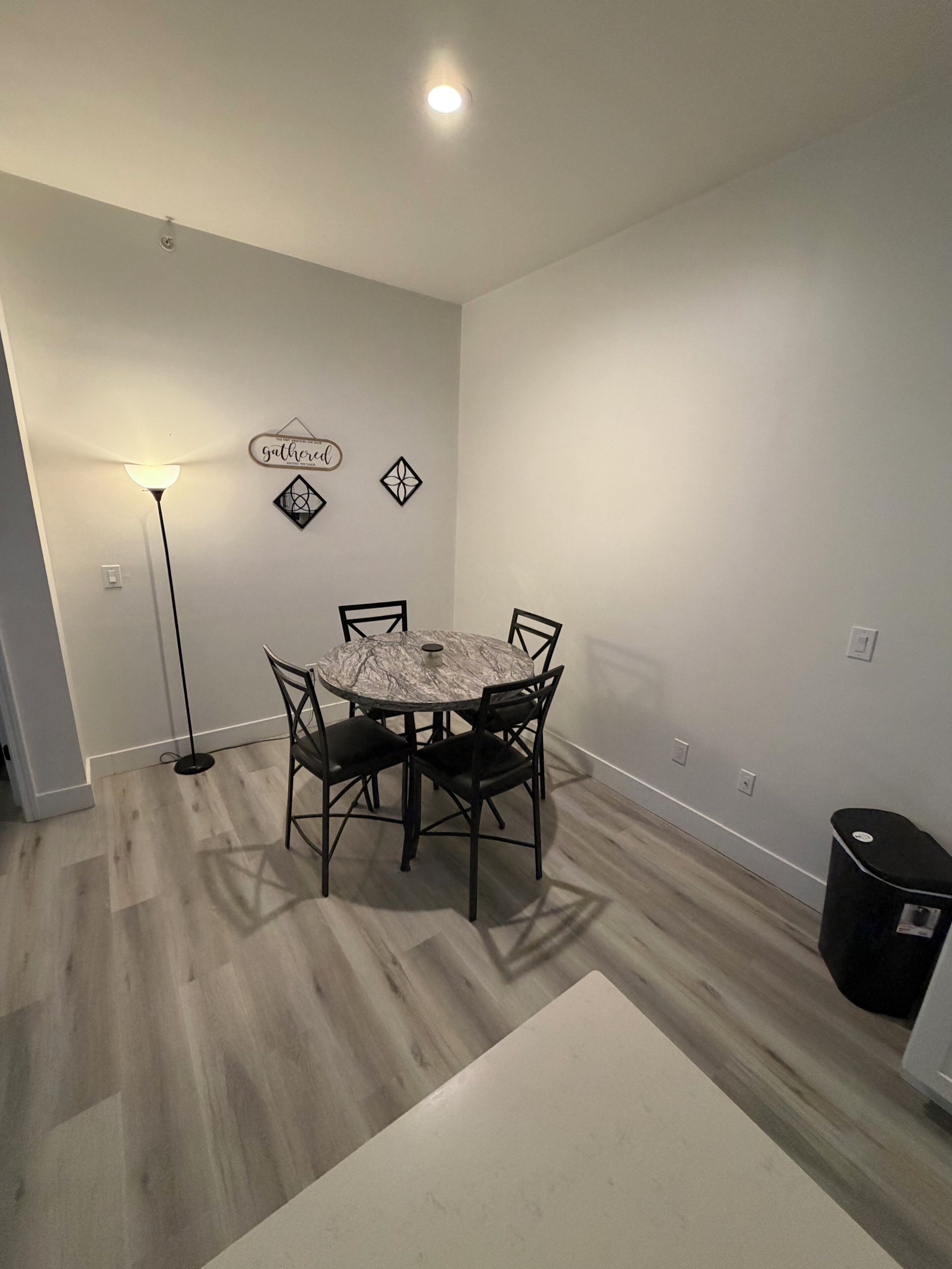 Un coin repas comprenant une table ronde, quatre chaises, un lampadaire et une poubelle.