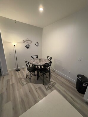 A dining area with a round table, four chairs, a floor lamp, and a trash bin. - Delightful 2-bedroom apartment with AC in Summerville (Summerville)