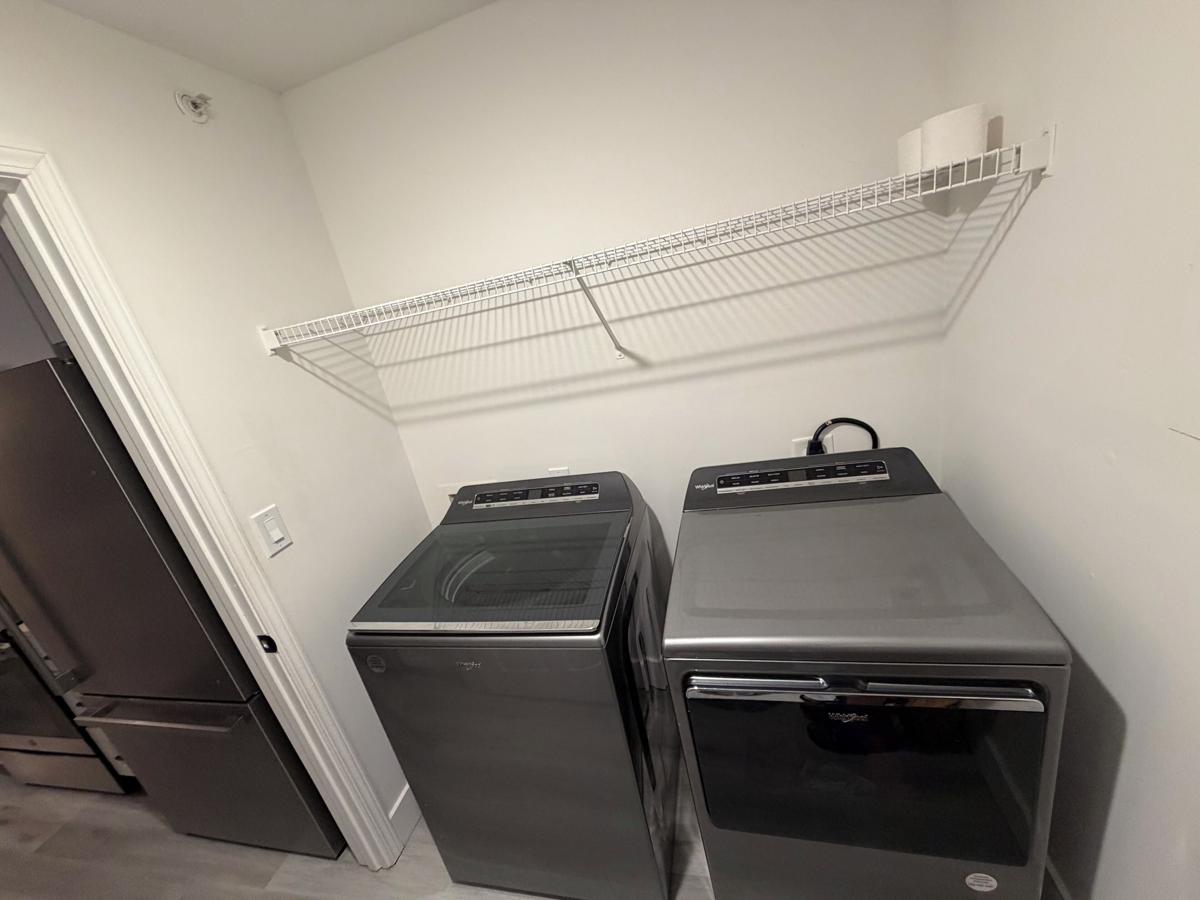 A laundry room with two stacked washer-dryer units and a metal shelf above.
