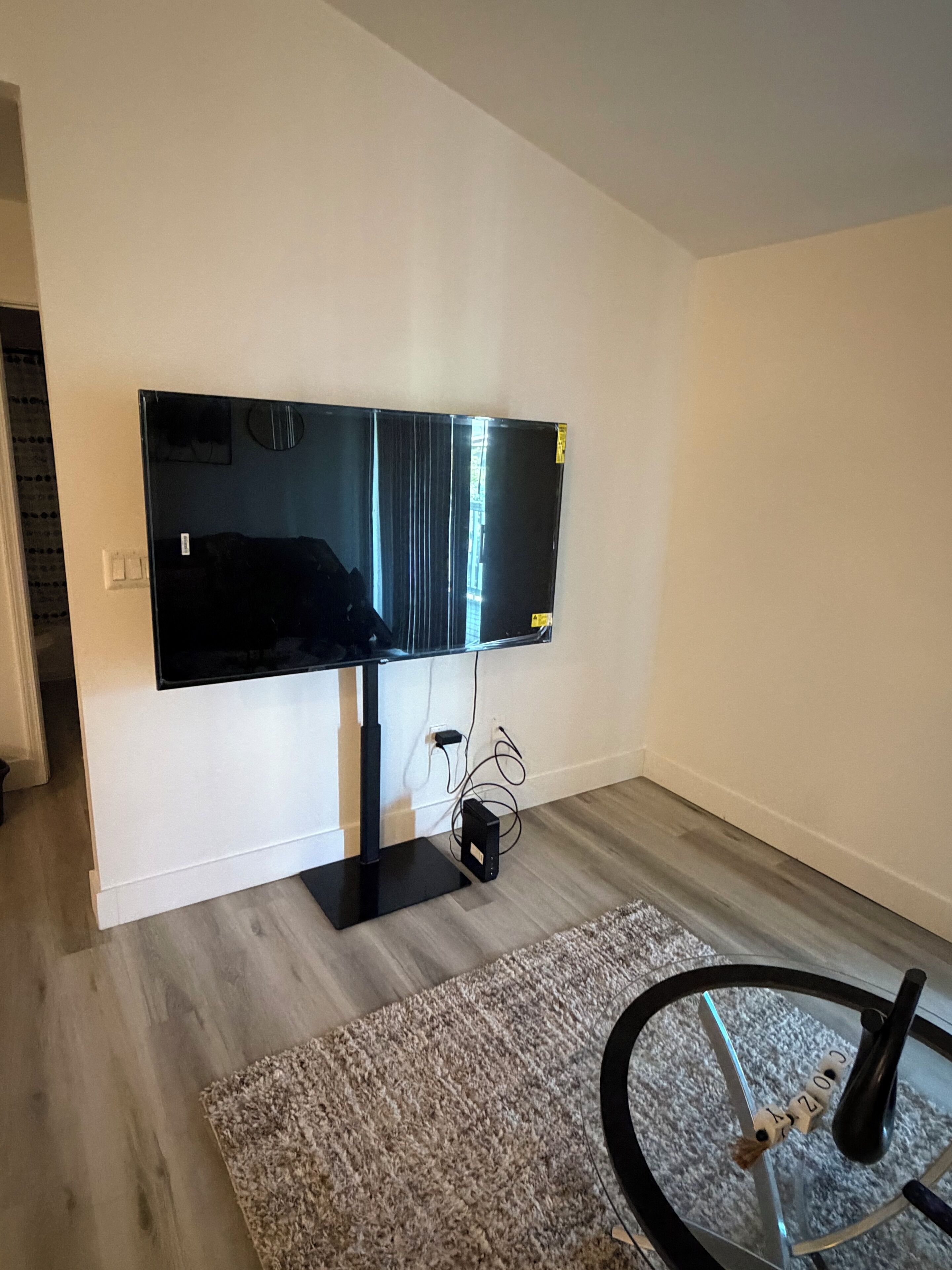 A room with a large flat-screen TV mounted on the wall, a small table with a vase, and a rug on the floor.