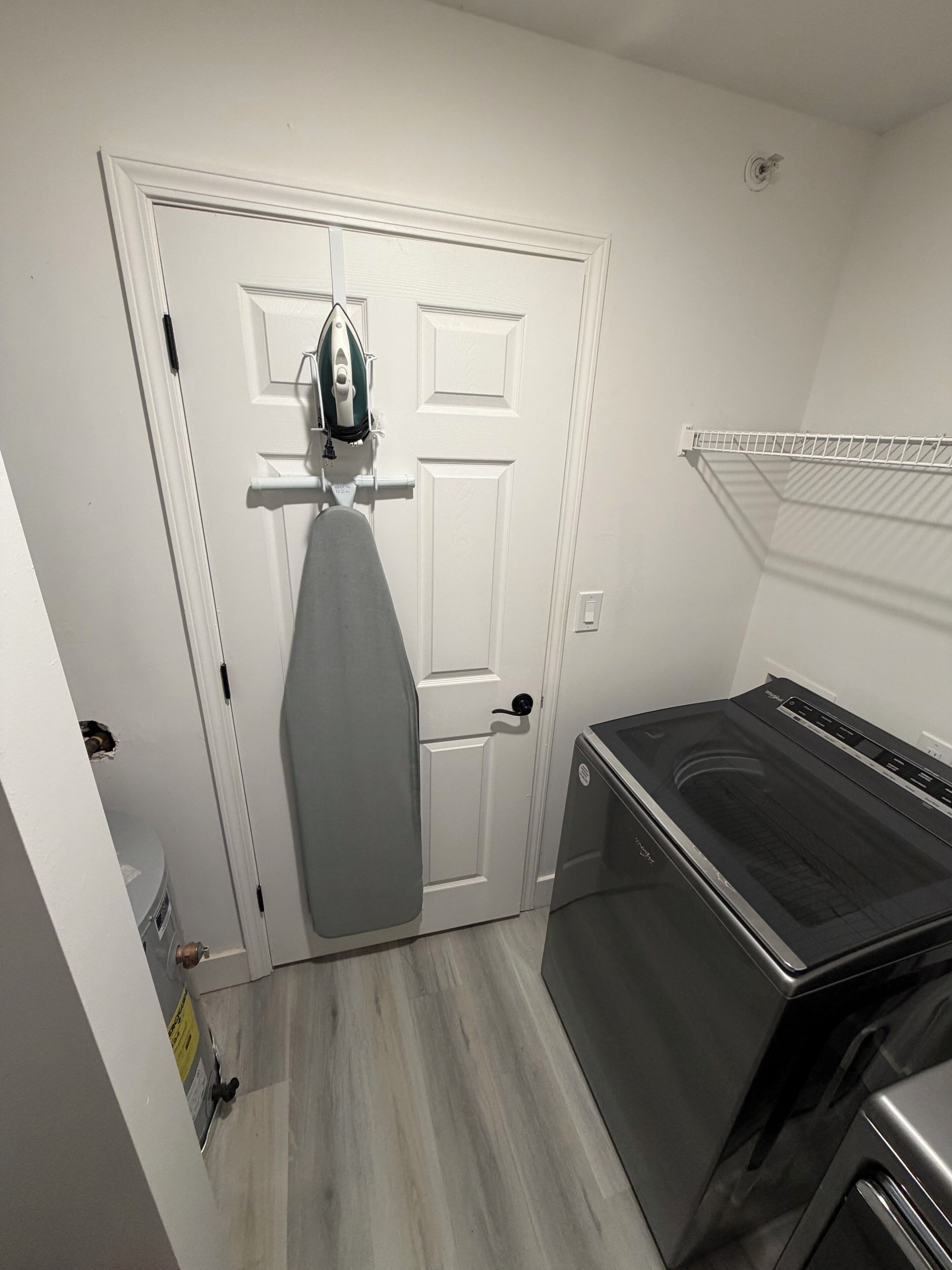 Un lavadero con lavadora y secadora, una puerta con un plancha colgada, y una pared blanca.