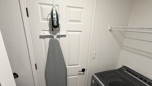 Ein Waschraum mit Waschmaschine und Trockner, einer Tür mit gebügeltem Bügeleisen und einer weißen Wand.
