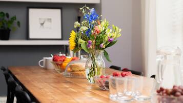 A wooden table with a vase of flowers, a bowl of strawberries, a pitcher, and a glass pitcher.