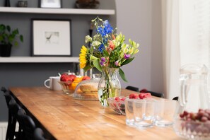 A wooden table with a vase of flowers, a bowl of strawberries, a pitcher, and a glass pitcher.