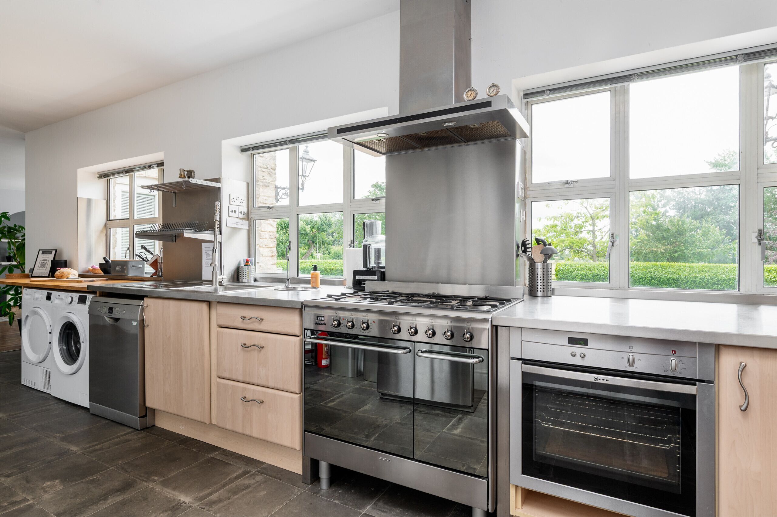 A modern kitchen with stainless steel appliances, a built-in oven, and a large window overlooking a garden.
