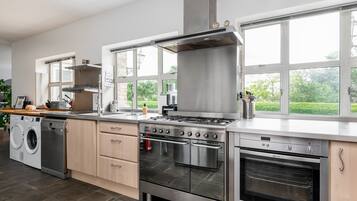 A modern kitchen with stainless steel appliances, a built-in oven, and a large window overlooking a garden.