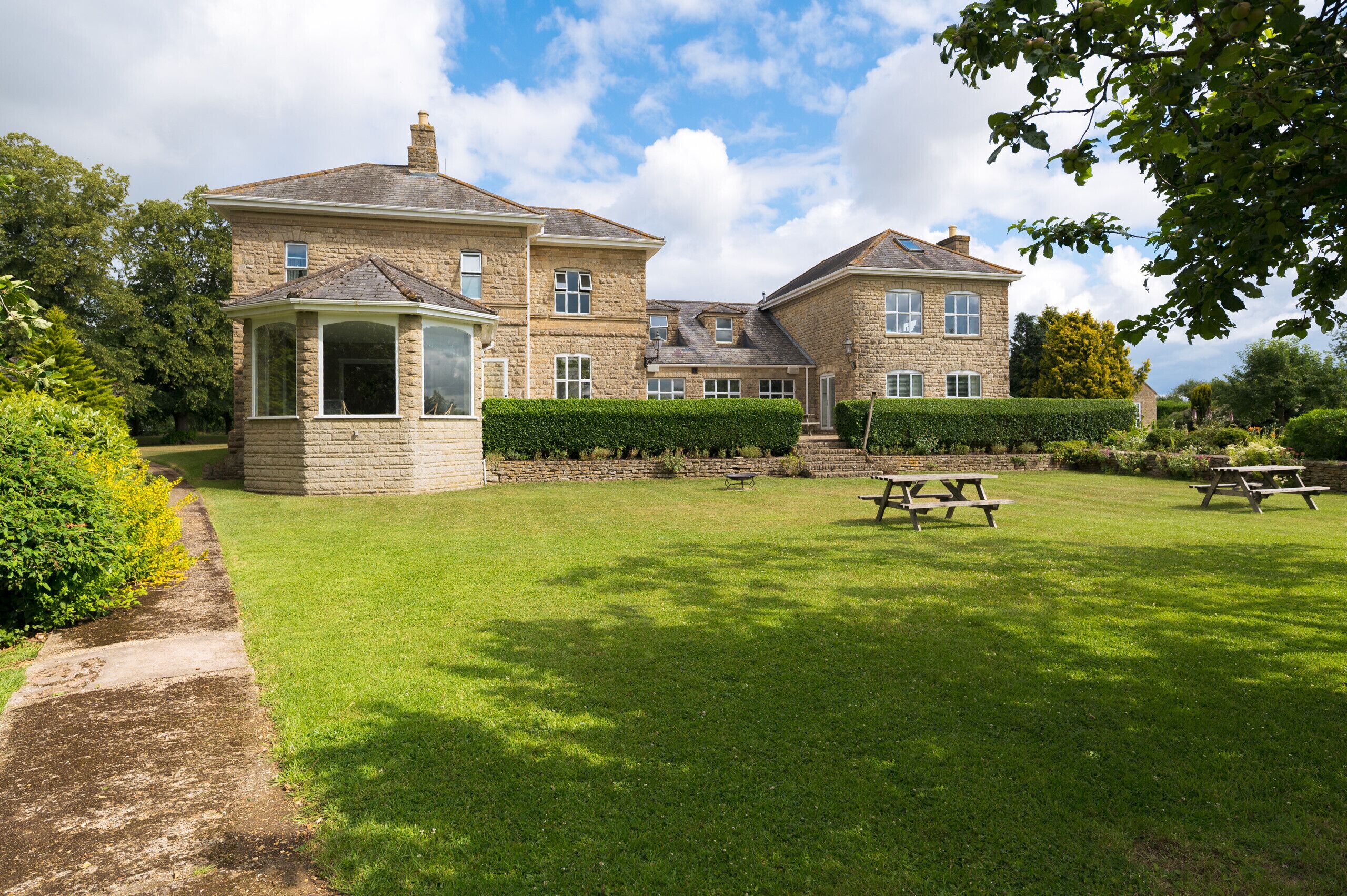 A stone building with a conservatory, a lawn, and picnic tables.