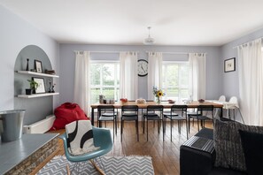 A dining area with a table, chairs, a clock, and a window with curtains.