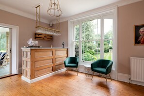 A kitchen with wooden cabinetry, a bar area, two green chairs, and large windows with a view of greenery.