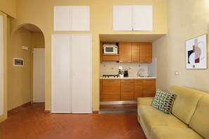 A compact kitchen with white cabinets, a microwave, and a stove. There is a yellow sofa with a patterned pillow and a tiled backsplash. - Just a short walk from the Ponte Vecchio, away from the noise (Firenze)