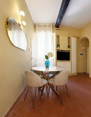 A dining area with a round table, four chairs, a vase with a single flower, a large mirror, and a television on a cabinet. - Just a short walk from the Ponte Vecchio, away from the noise (Firenze)