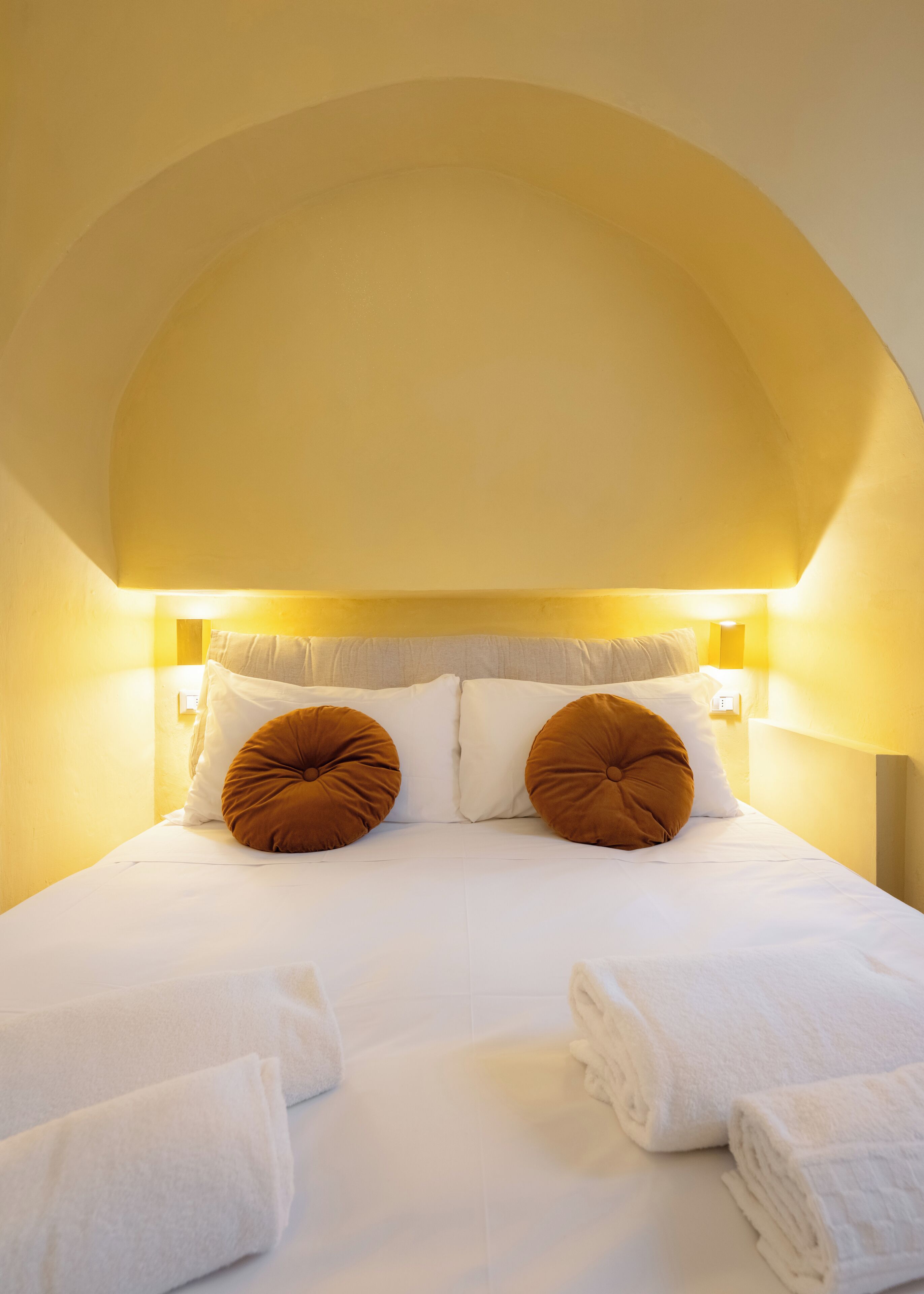 A hotel room with a bed, two pillows, and a headboard.