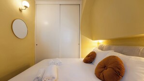 Una habitación de hotel con cama, una puerta blanca, un espejo redondo y una lámpara fijada a la pared.