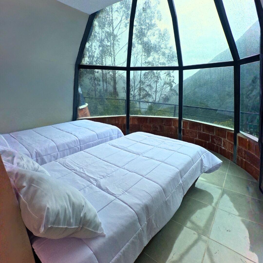 Una habitación con una cama grande, un ventanal con vistas a árboles y una pared de ladrillo.