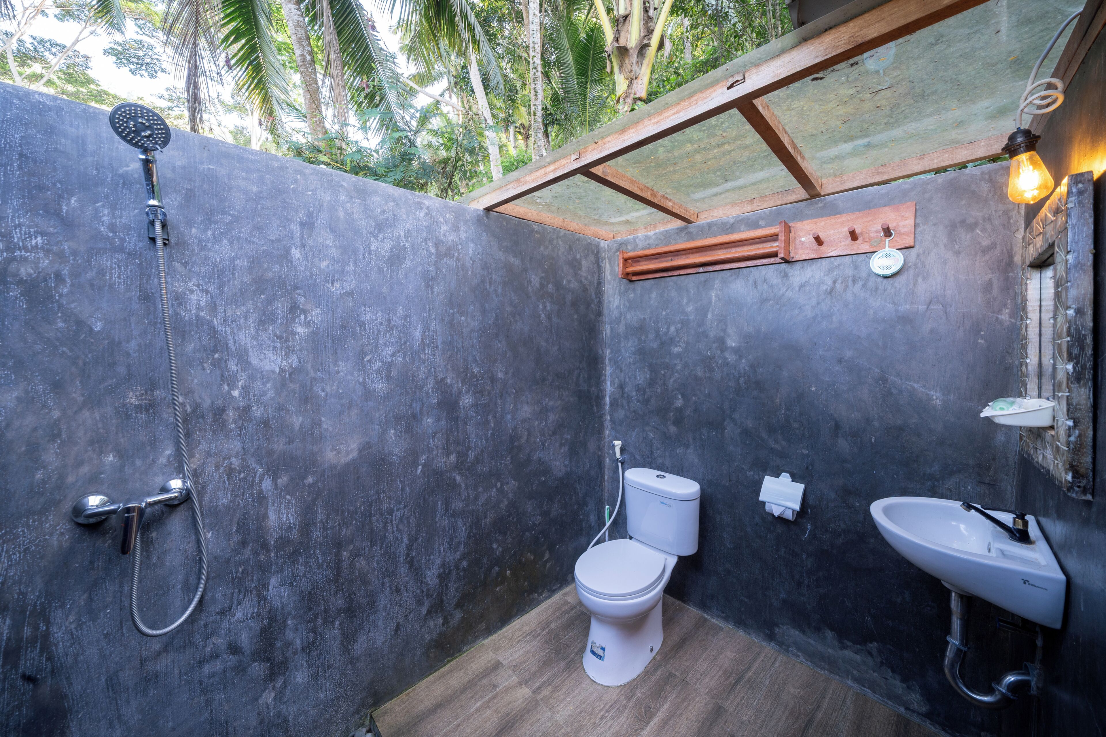 Une petite salle de bain comprenant une douche, des toilettes et un lavabo, avec un mur en béton et des éléments décoratifs en bois.