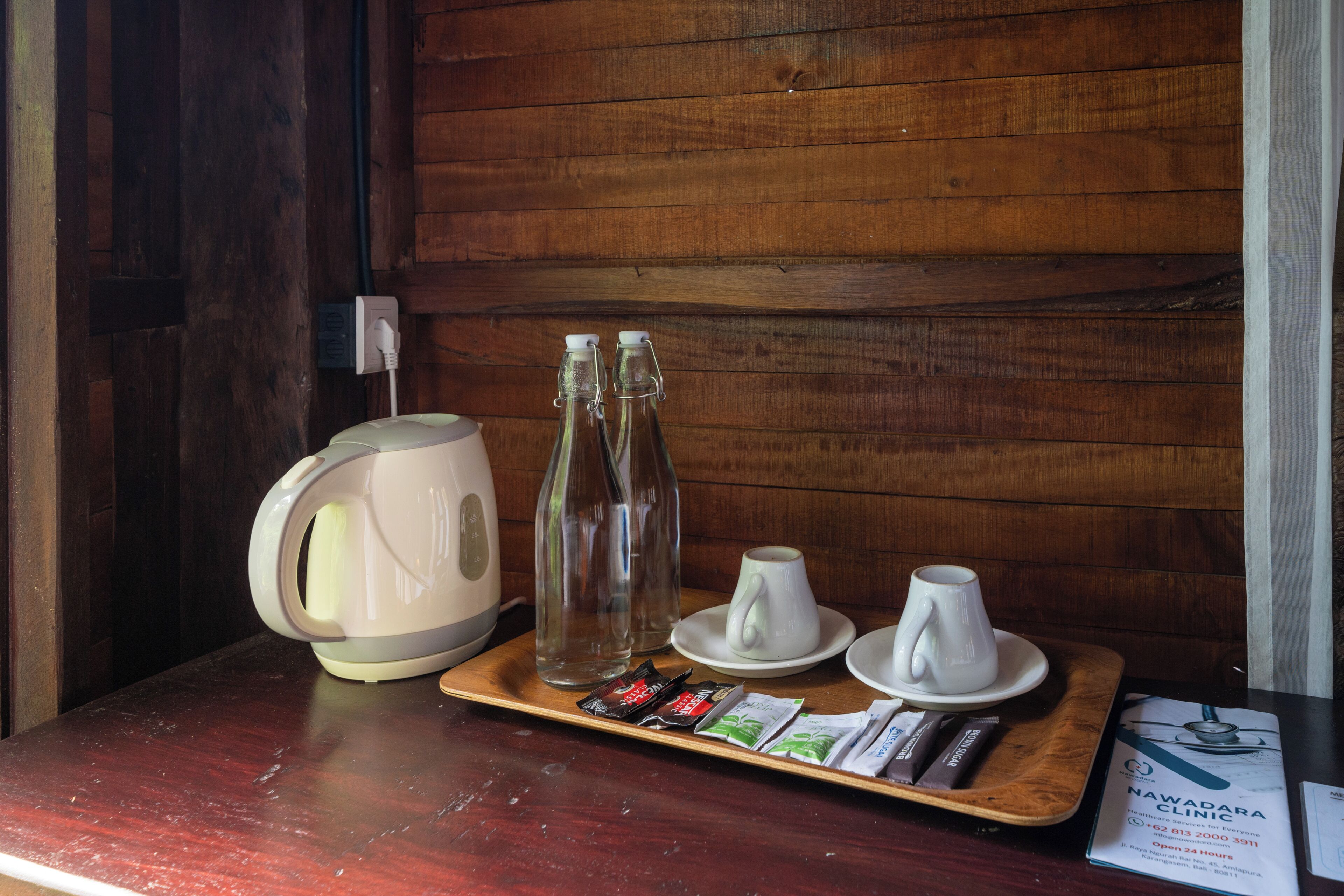 A wooden table with a kettle, two glass bottles, two white cups, and some packaged snacks.