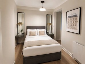 Un dormitorio moderno de hotel con una cama grande, dos mesitas de noche con lámparas, una obra de arte con un dibujo urbano enmarcado y un radiador.