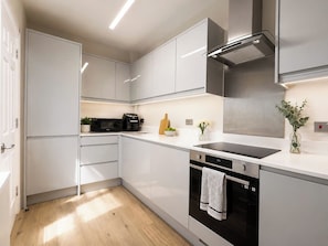 Una cocina moderna con muebles blancos, un lavavajillas negro y una campana extractora de acero inoxidable.