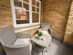 Una habitación de esquina con dos sillones de mimbre, una mesita y un ventanal.