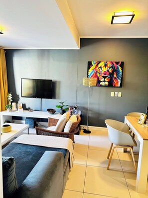 A modern living room with a flat-screen TV, a painting, a dining area, and a seating arrangement. - Stylish 2-Bed Apartment with Pool, Gym & Mountain Views. Walk to V&A Waterfront! (Cape Town)